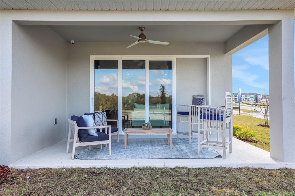 A covered patio features a ceiling fan, sliding glass doors, and outdoor furniture on a rug — 5361 SPADERDOCK LANE, APOPKA, FL