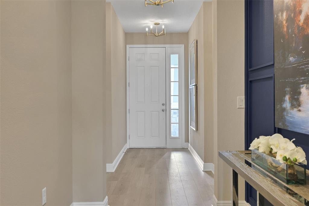 A bright entryway features light wood flooring, beige walls, a white front door, and blue accents — 5361 SPADERDOCK LANE, APOPKA, FL