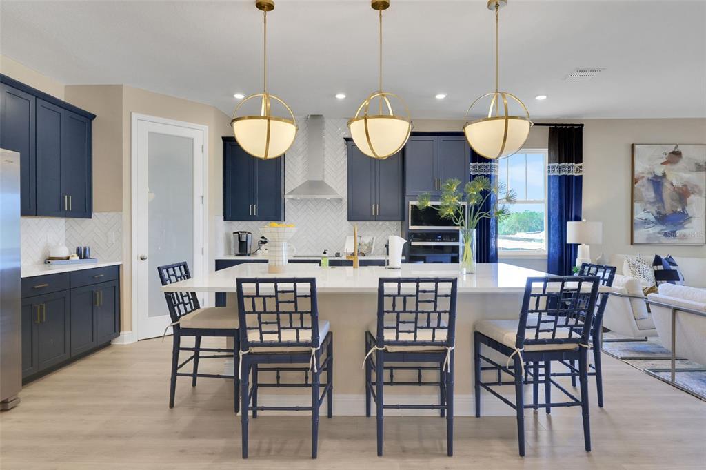 A kitchen features dark blue cabinets, a white island with three chairs, and gold pendant lights — 5361 SPADERDOCK LANE, APOPKA, FL