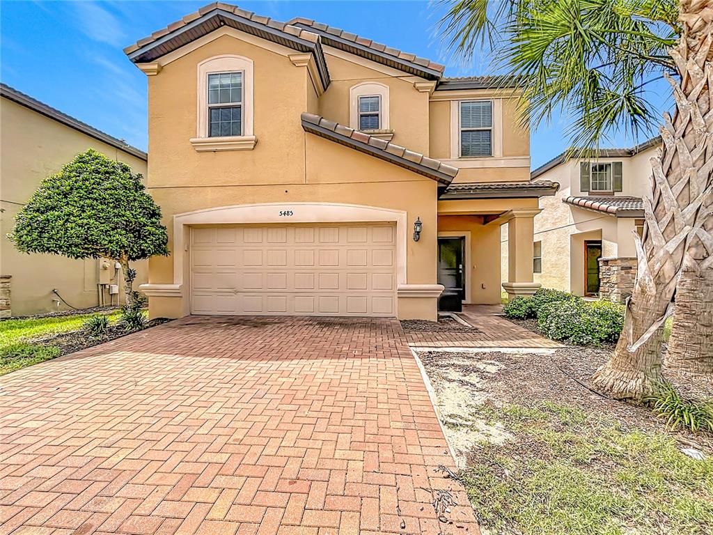 A two-story tan stucco house with a brick paver driveway and a two-car garage — 5485 MISTY OAK CIRCLE, DAVENPORT, FL