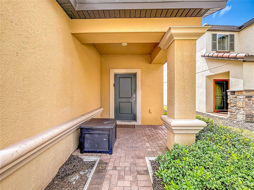 A covered entryway features a gray front door, a brick paver porch, and stucco walls — 5485 MISTY OAK CIRCLE, DAVENPORT, FL