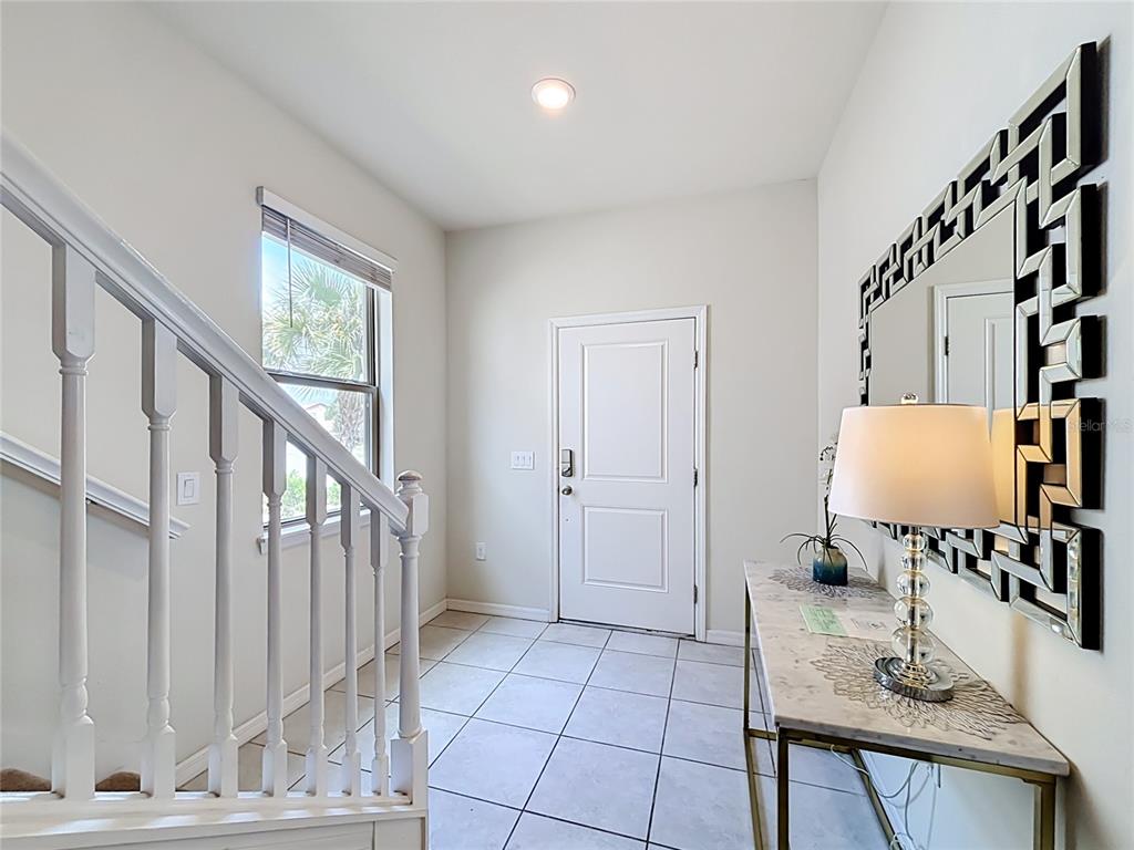 An entryway features white tile flooring, a staircase with white railings, and a decorative wall mirror — 5485 MISTY OAK CIRCLE, DAVENPORT, FL