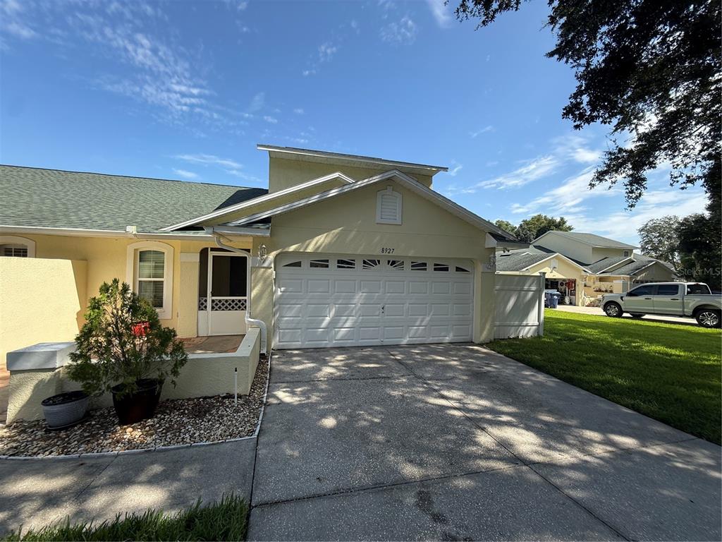 A pale yellow house features a two-car garage, a front patio, and a concrete driveway — 8927 COURTYARD LANE, GROVELAND, FL