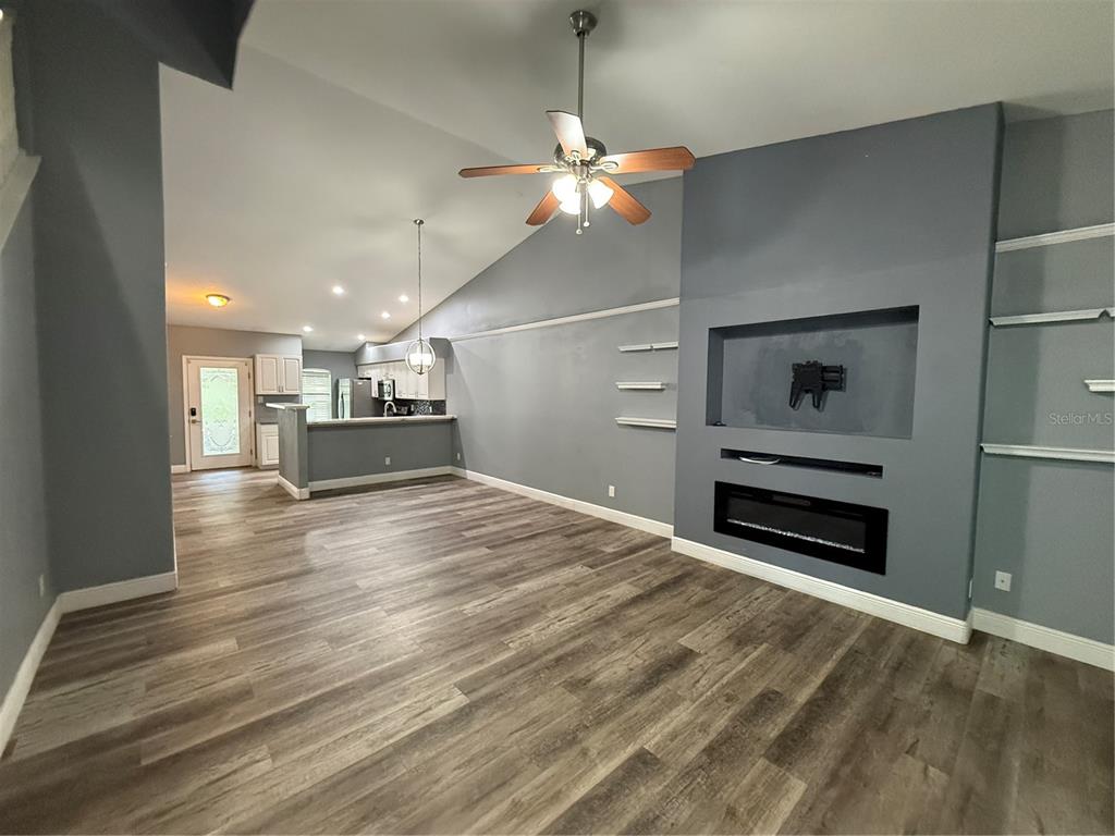 A living room with wood-look flooring, a fireplace, built-in shelving, and an adjacent kitchen — 8927 COURTYARD LANE, GROVELAND, FL