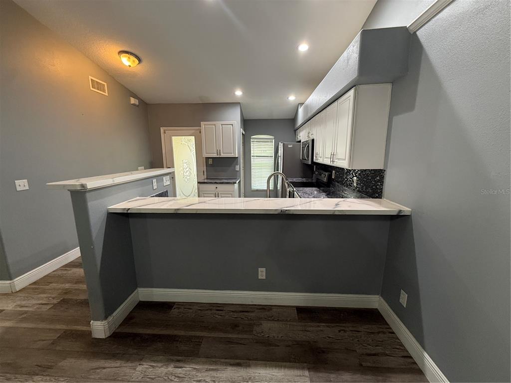 A kitchen features white cabinets, a marble-look breakfast bar, and gray walls over wood flooring — 8927 COURTYARD LANE, GROVELAND, FL