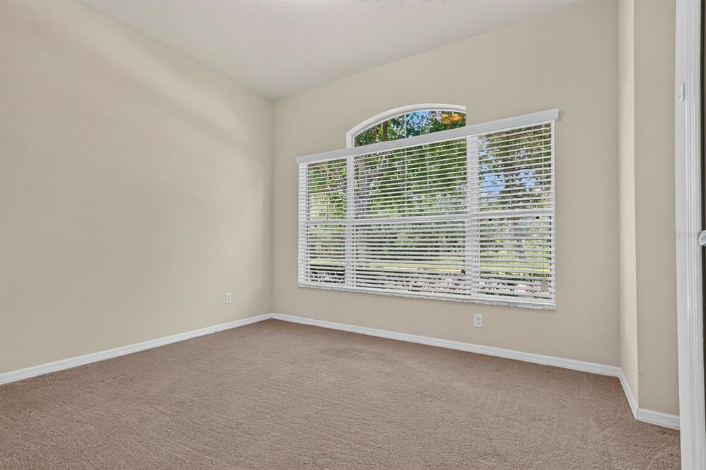 An empty room with beige walls, brown carpet, and a large arched window with blinds — 11231 BELLE HAVEN DRIVE, NEW PORT RICHEY, FL