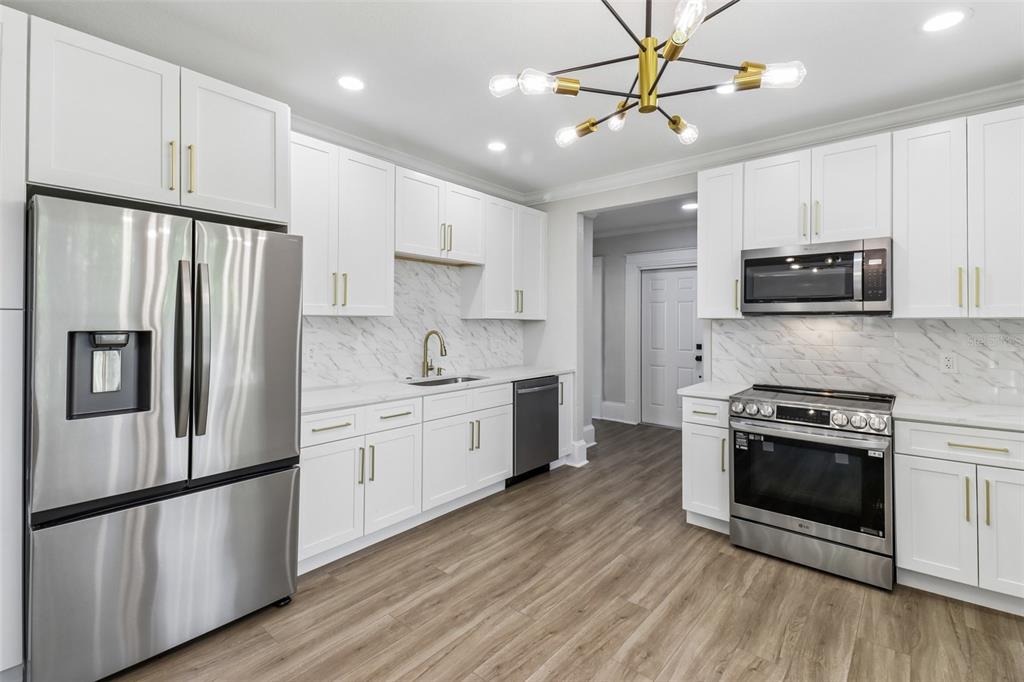 A modern kitchen features white cabinets, stainless steel appliances, and light wood-look flooring — 43 W MURIEL STREET, ORLANDO, FL
