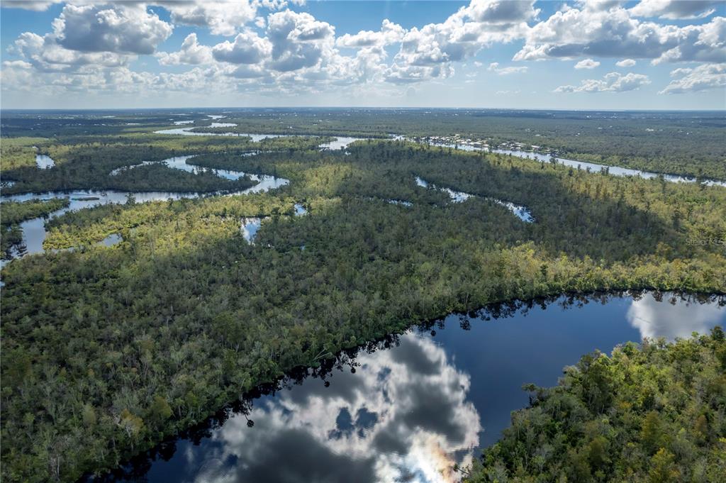 An aerial view shows a winding river flowing through a dense, forested landscape under clouds — SW CO ROAD 761 UNIT A, ARCADIA, FL