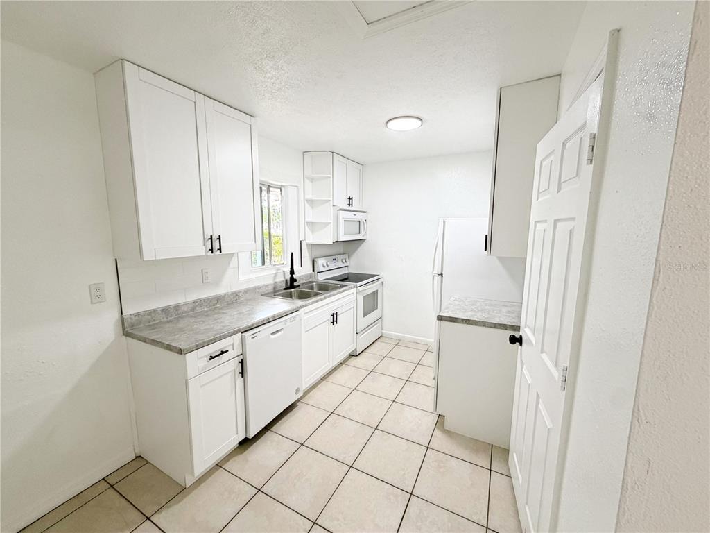 A white kitchen features gray laminate countertops, white cabinetry, and light-colored tile flooring — 3916 E GENESEE STREET, TAMPA, FL