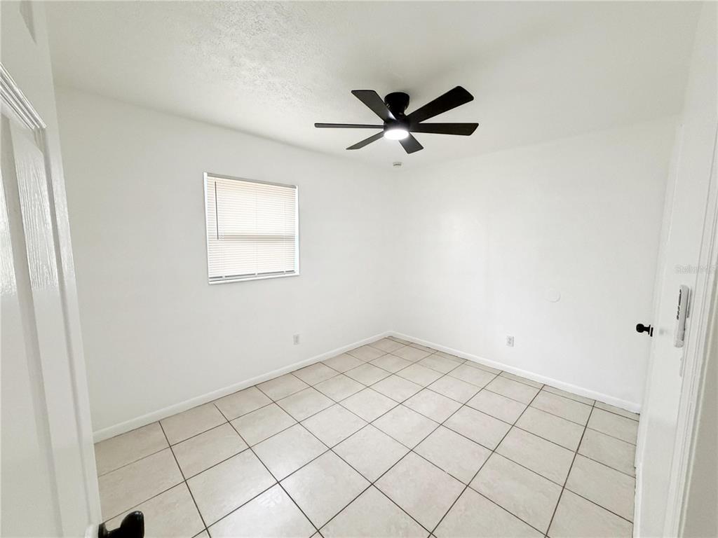 A small, empty bedroom features white walls, light-colored tile flooring, and a black ceiling fan — 3916 E GENESEE STREET, TAMPA, FL