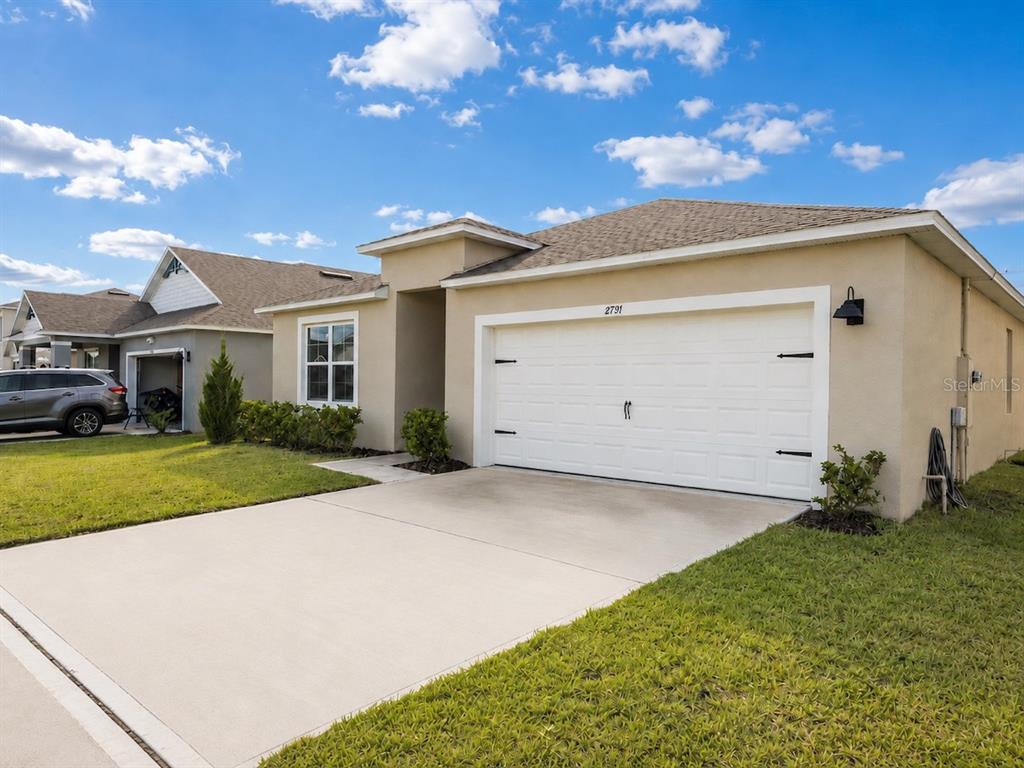 A tan single-story house with a white two-car garage and a concrete driveway — 2791 HOUSE FINCH ROAD, ST CLOUD, FL