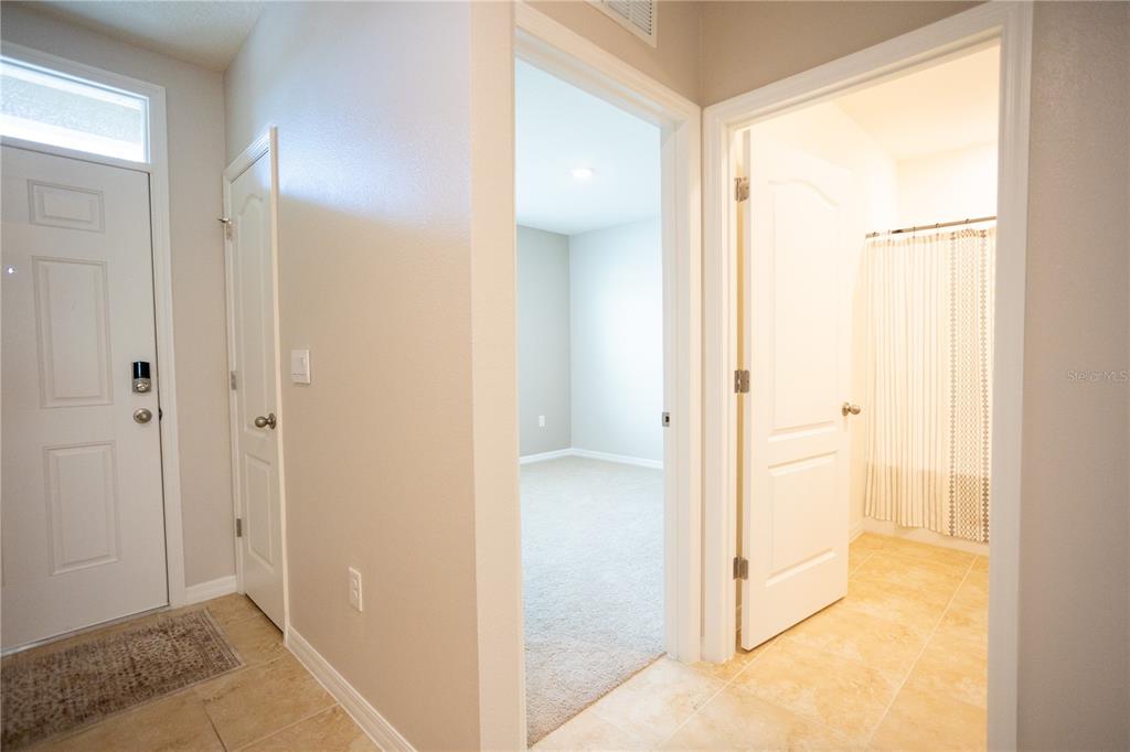 A hallway with tile flooring leads to a carpeted bedroom and a bathroom with a shower — 2791 HOUSE FINCH ROAD, ST CLOUD, FL