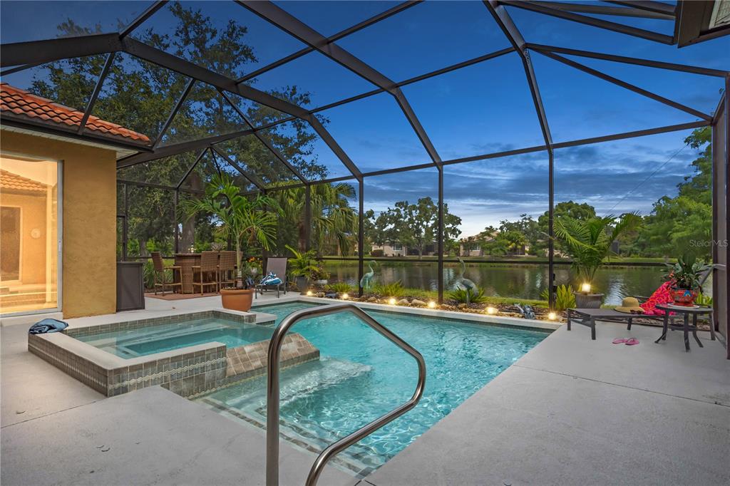 A screened-in pool and spa area overlooks a lake at dusk — 521 HABITAT BOULEVARD, OSPREY, FL