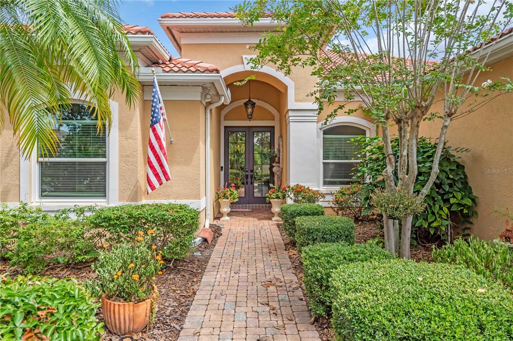 A brick walkway leads to the front entrance of a tan house with a tiled roof — 521 HABITAT BOULEVARD, OSPREY, FL