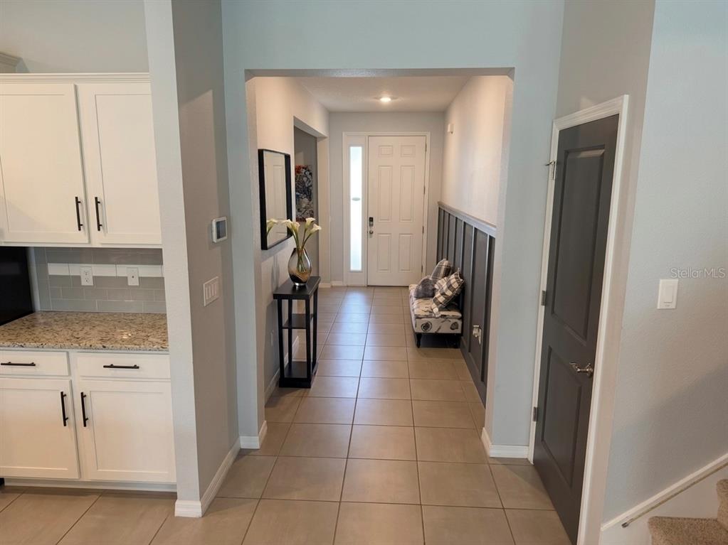 A tiled entryway features a white front door, a dark accent wall, and adjacent kitchen cabinetry — 16910 OVAL RUM DRIVE, WIMAUMA, FL
