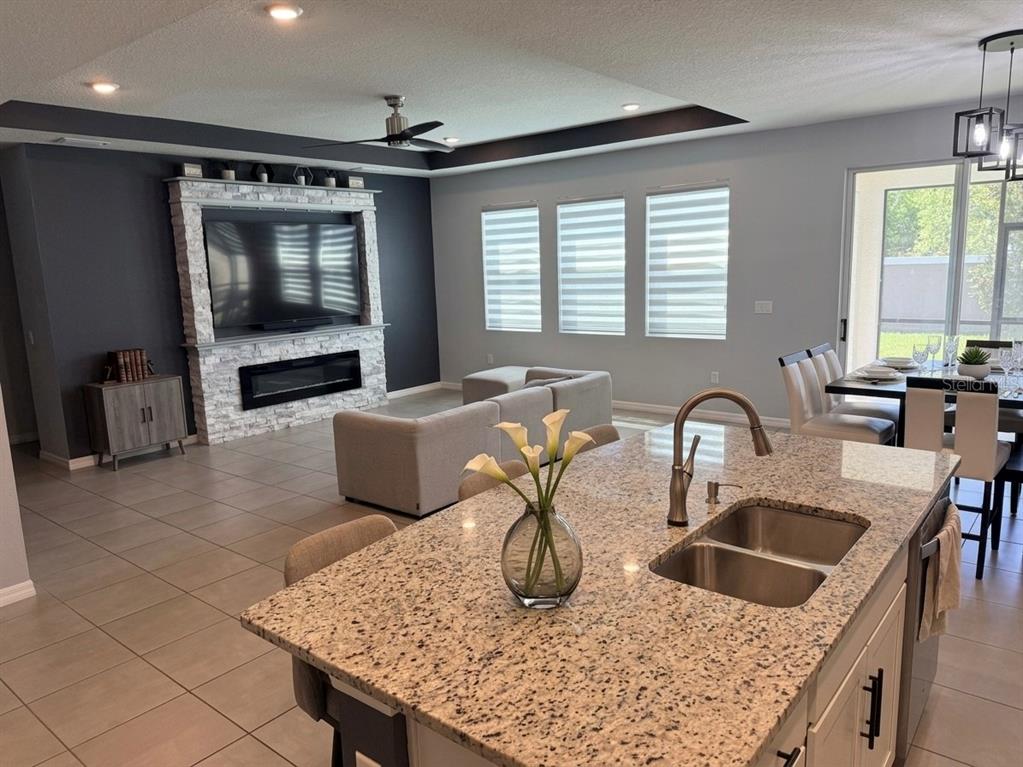 An open-concept kitchen with a granite island overlooks a living room featuring a stone fireplace — 16910 OVAL RUM DRIVE, WIMAUMA, FL