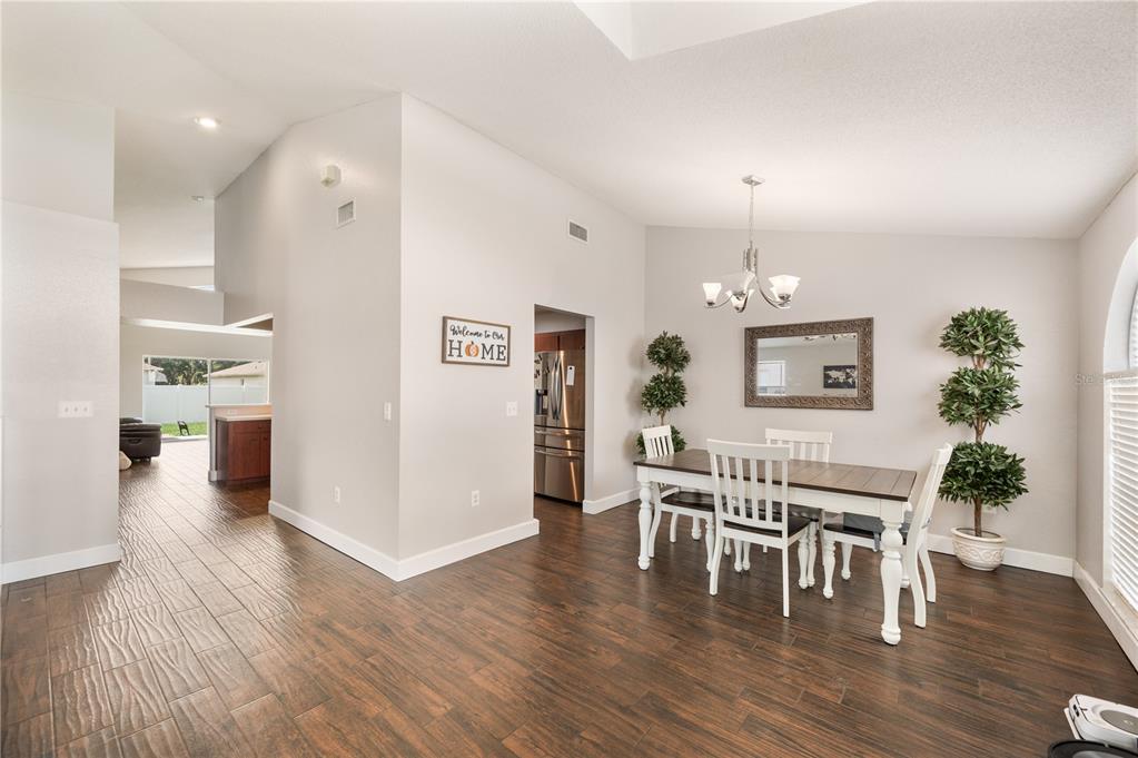 A dining area with a wooden table, white chairs, and dark wood-look tile flooring — 3326 MERLOT DRIVE, LAKELAND, FL