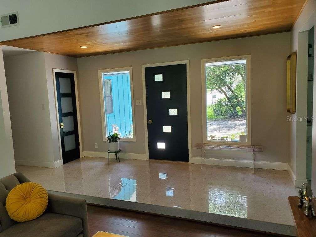An entryway features a raised terrazzo floor, a modern black front door, and wood-paneled ceilings — 5017 E 127TH AVENUE, TEMPLE TERRACE, FL