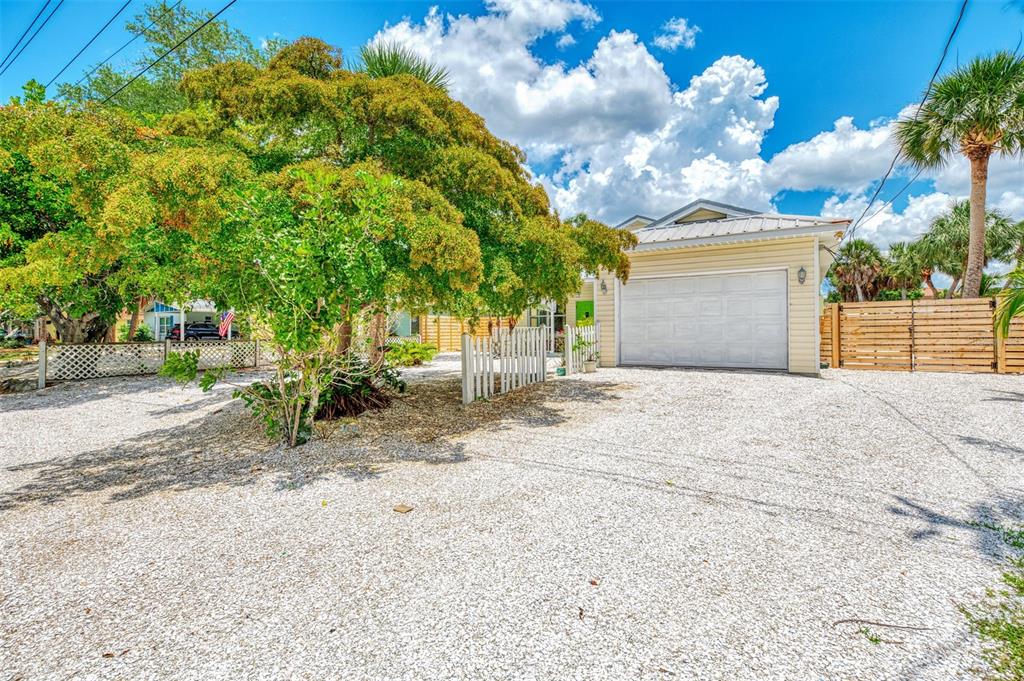 A gravel driveway leads to a house with a white garage door and a large tree — 5253 AVENIDA DEL MARE, SARASOTA, FL