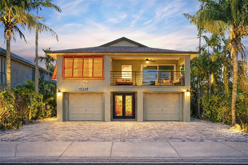 A two-story house with a balcony, two garage doors, and palm trees at dusk — 15517 GULF BOULEVARD, REDINGTON BEACH, FL