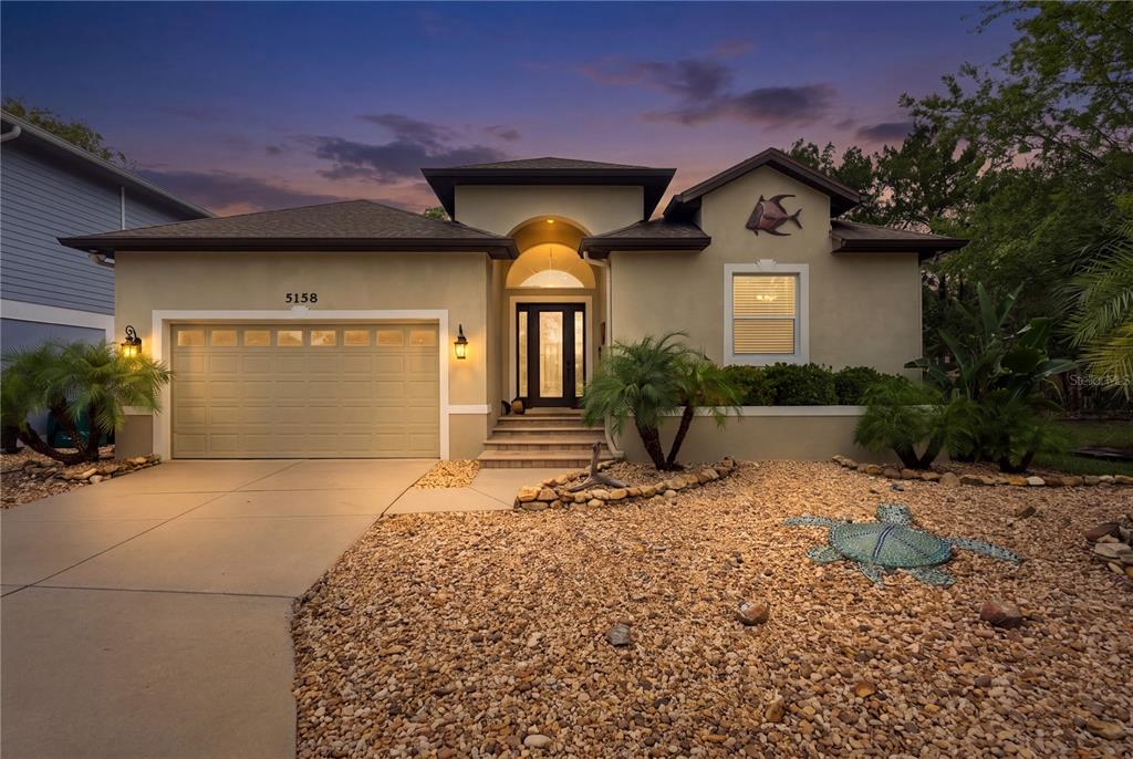 A single-story house with a beige stucco exterior, a two-car garage, and a gravel front yard — 5158 S RIVERVIEW CIRCLE, HOMOSASSA, FL