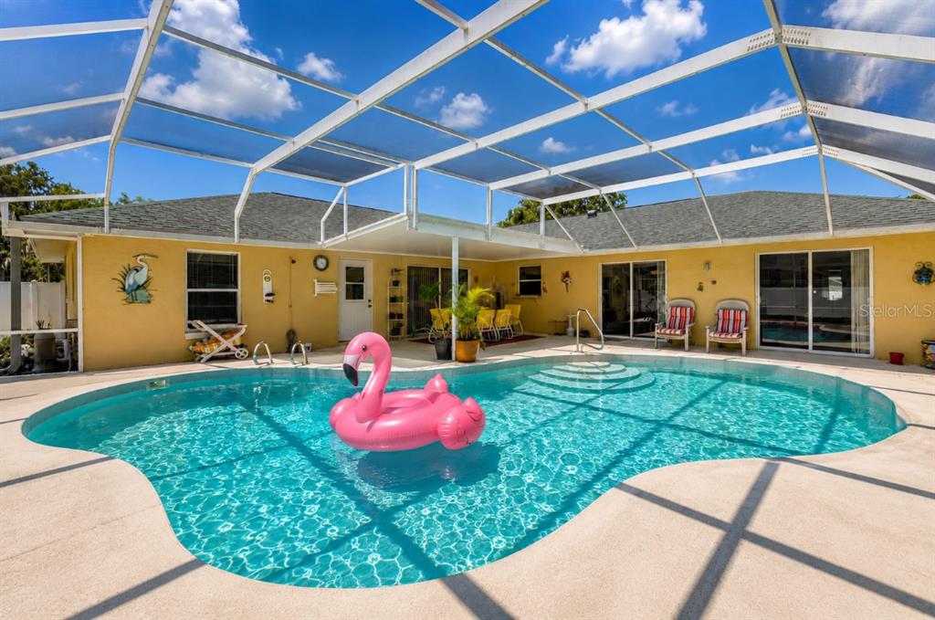 A swimming pool with a pink flamingo float sits inside a screened-in patio area — 1529 SABAL PALM DRIVE, EDGEWATER, FL