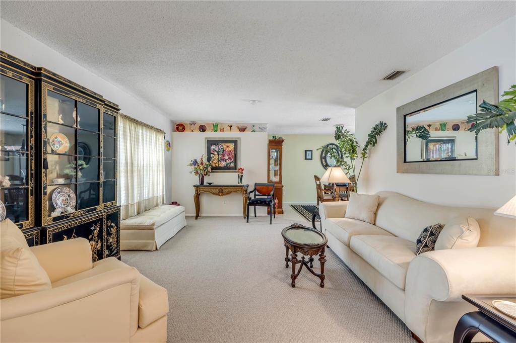 A living room features a beige sofa, an armchair, a black display cabinet, and carpeted floors — 1529 SABAL PALM DRIVE, EDGEWATER, FL