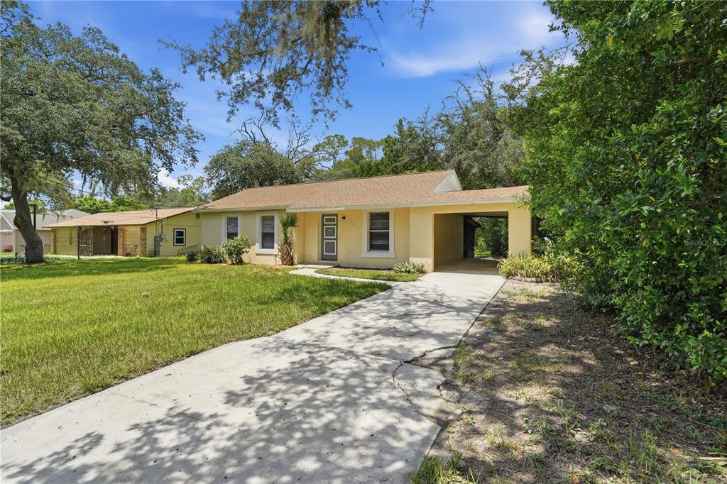 A single-story yellow house with a concrete driveway and an attached carport under a tree — 336 RIVIERA DRIVE, DEBARY, FL