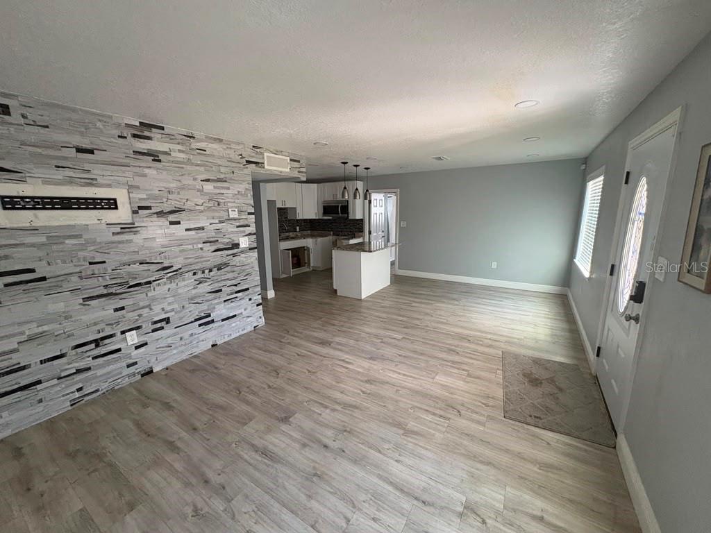A living room with wood-look flooring and a gray stone accent wall leads to a kitchen — 3206 E EMMA STREET, TAMPA, FL