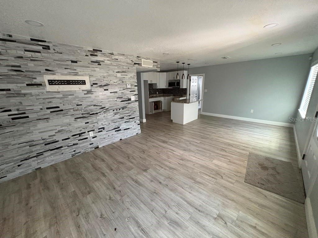 An open-concept living area features a stone-accented wall, light wood flooring, and a kitchen island — 3206 E EMMA STREET, TAMPA, FL
