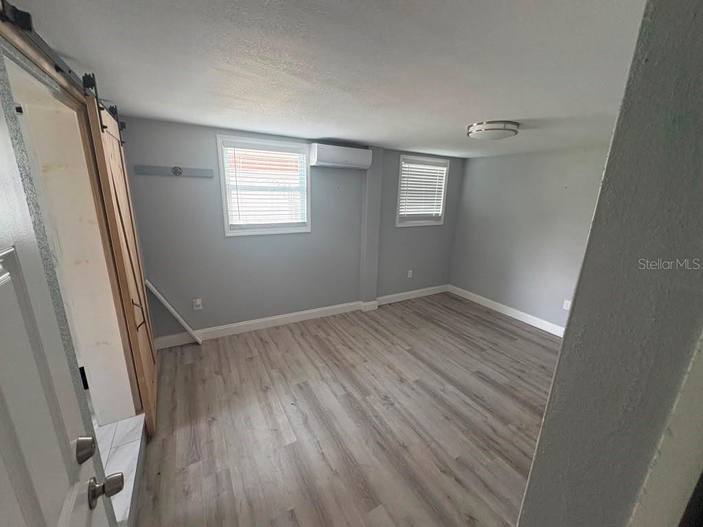 An empty room features gray walls, wood-look flooring, two windows, and a wall-mounted air conditioner — 3206 E EMMA STREET, TAMPA, FL