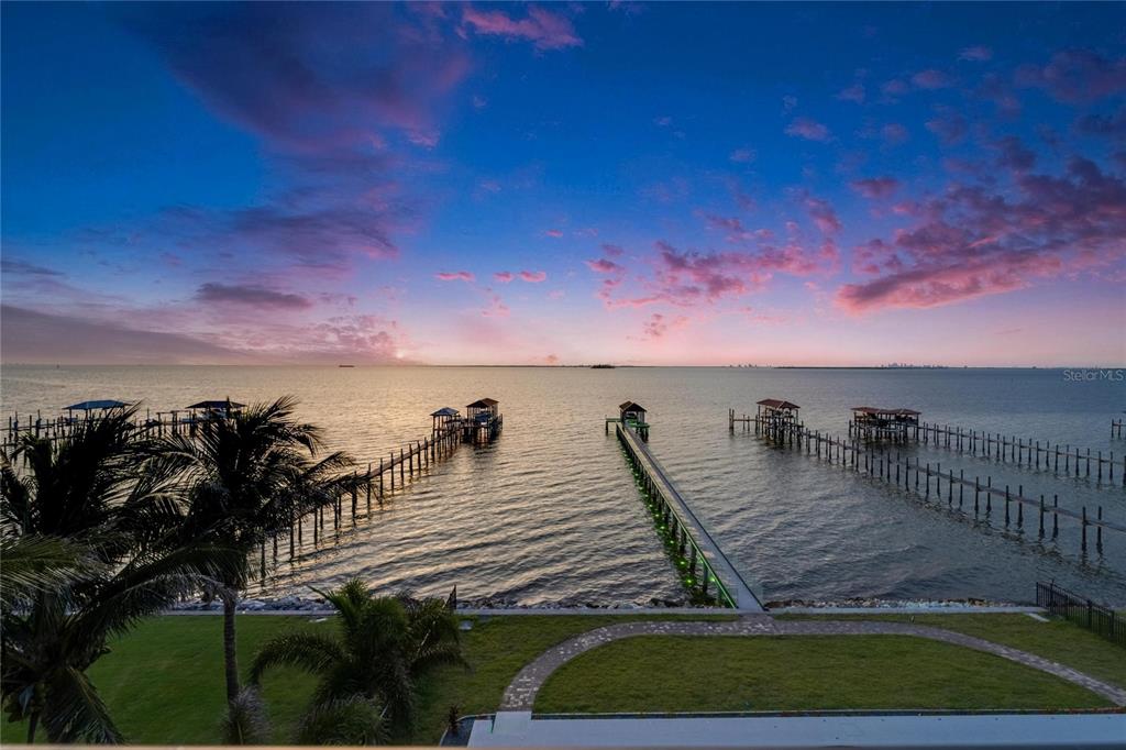 An elevated view of a grassy lawn, stone walkway, and multiple wooden docks at sunset — 6526 SURFSIDE BOULEVARD, APOLLO BEACH, FL