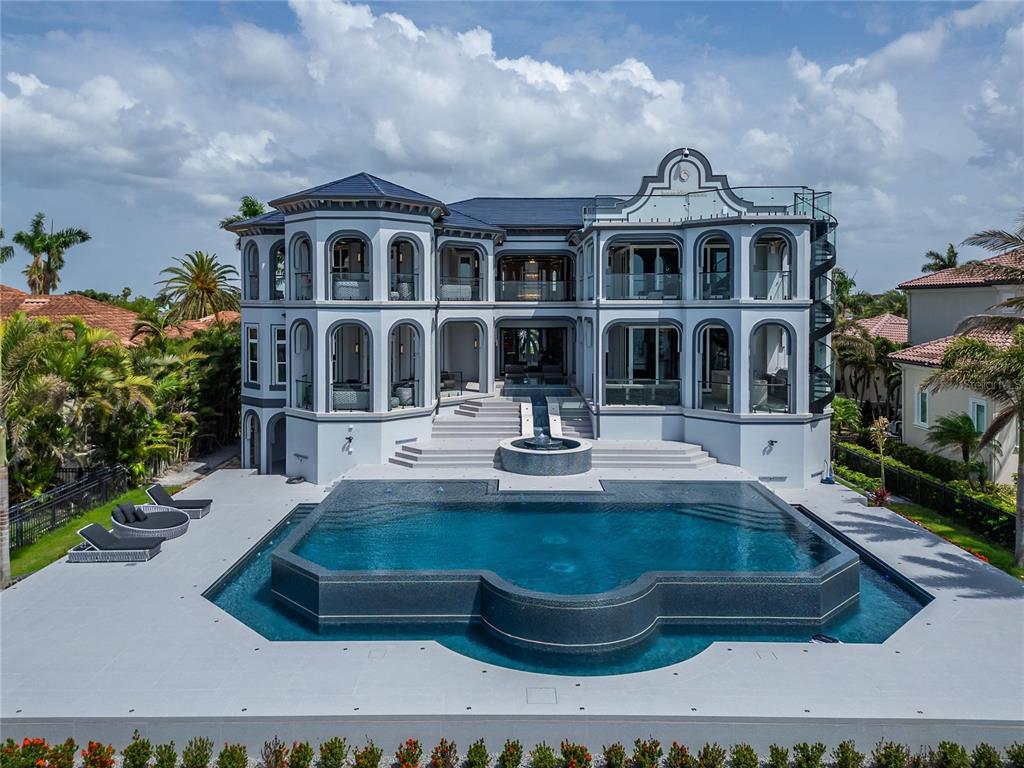 A large, multi-story gray mansion features a custom-shaped swimming pool and a central fountain — 6526 SURFSIDE BOULEVARD, APOLLO BEACH, FL