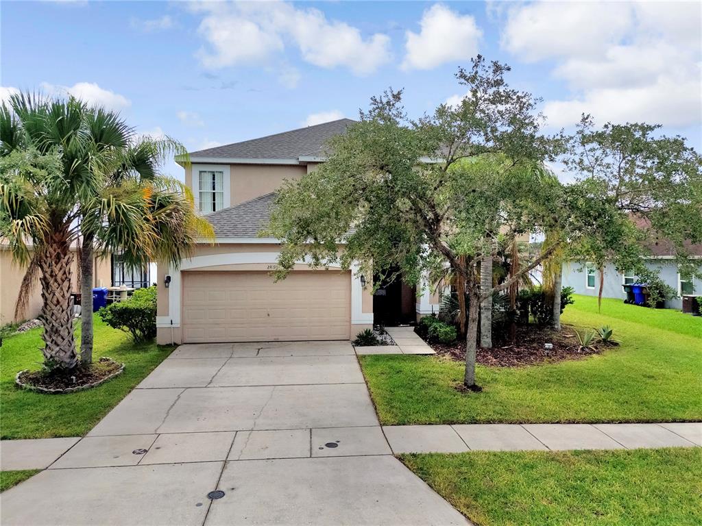 A two-story beige house with a two-car garage, a concrete driveway, and mature landscaping — 2803 BOATING BOULEVARD, KISSIMMEE, FL