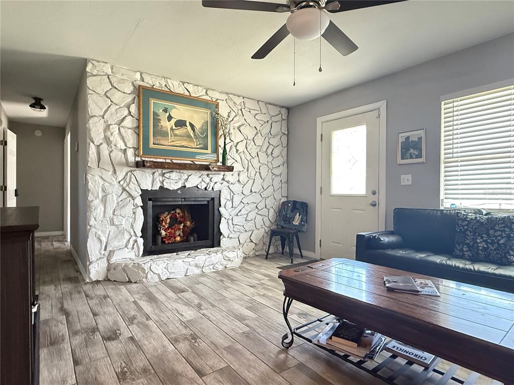 A living room features a white stone fireplace, wood-look tile flooring, and a ceiling fan — 6809 NW 60TH STREET, OCALA, FL
