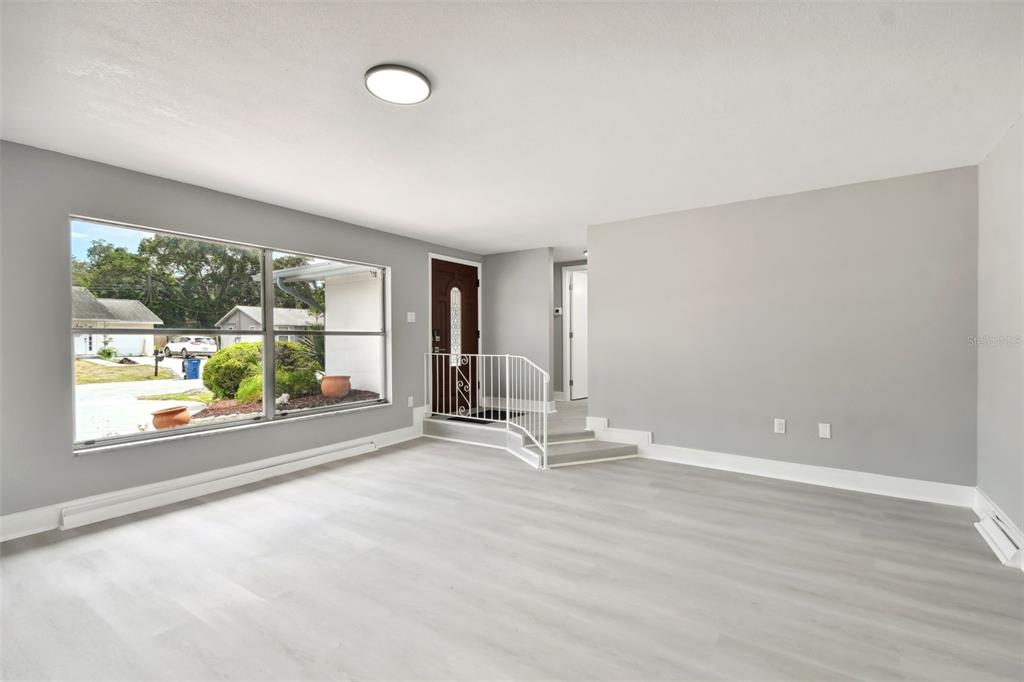A living room with light gray walls, wood-look flooring, a large window, and a front door — 4411 3RD AVENUE E, BRADENTON, FL