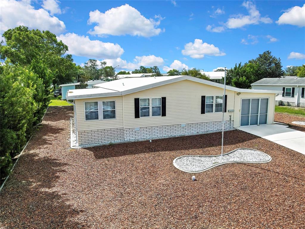An exterior view of a light-colored manufactured home with a gravel yard and flagpole — 14992 RIALTO AVENUE, BROOKSVILLE, FL