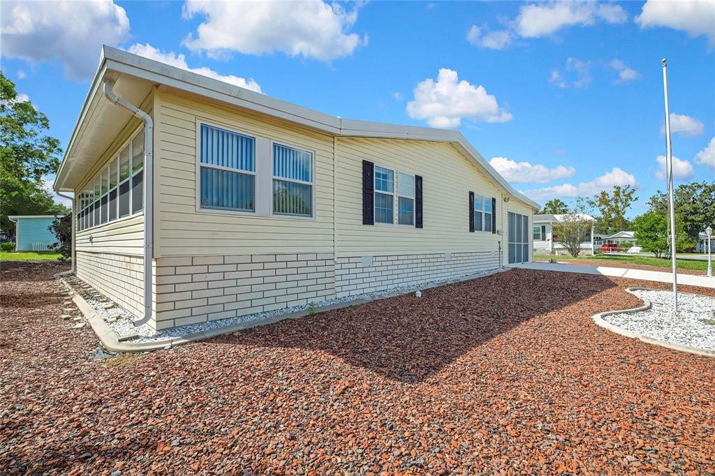 The exterior of a light yellow manufactured home features brick skirting and a gravel yard — 14992 RIALTO AVENUE, BROOKSVILLE, FL