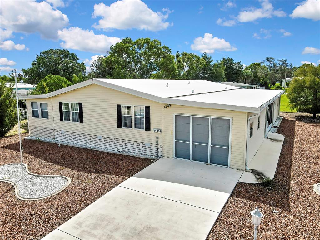 A single-story mobile home with light yellow siding, a white roof, and a concrete driveway — 14992 RIALTO AVENUE, BROOKSVILLE, FL