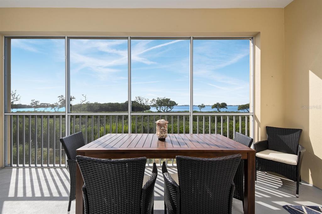 A screened-in balcony features a wooden dining table with chairs overlooking a water view — 384 ARUBA CIRCLE UNIT 102, BRADENTON, FL