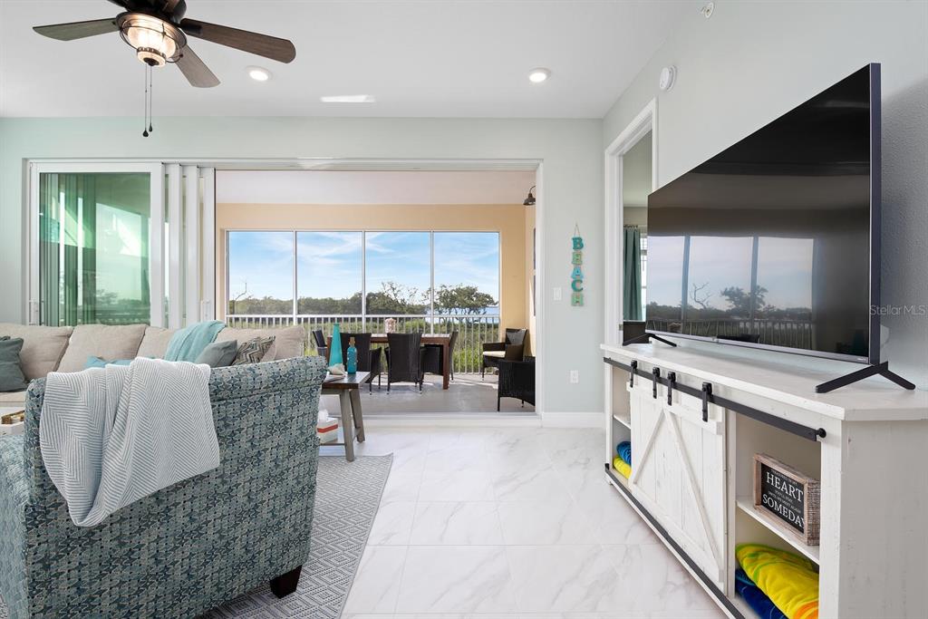 A living room features a large television, a white media console, and sliding doors to a balcony — 384 ARUBA CIRCLE UNIT 102, BRADENTON, FL