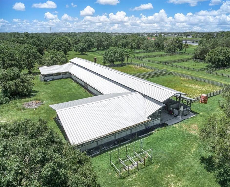 An aerial view of an L-shaped metal-roofed barn situated on a large grassy rural property — 4567 HIGHWAY 710, OKEECHOBEE, FL