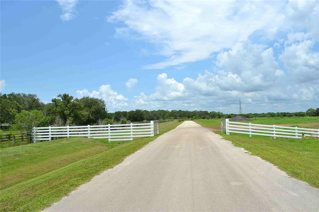 A paved driveway leads through a white fence into a large, open grassy field — 4567 HIGHWAY 710, OKEECHOBEE, FL