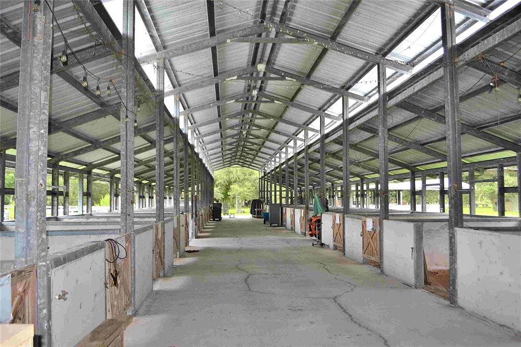 A long, open-air horse stable with a concrete aisle and multiple stalls on both sides — 4567 HIGHWAY 710, OKEECHOBEE, FL