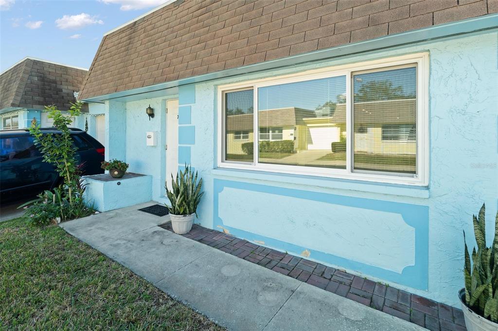 A light blue exterior wall features a large window, a front door, and a walkway — 7050 VERSAILLES N, PINELLAS PARK, FL