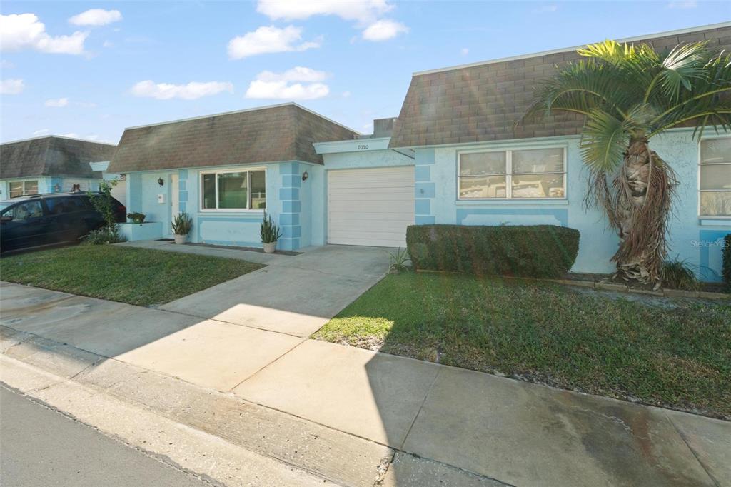 A light blue single-story house features a white garage door and a palm tree — 7050 VERSAILLES N, PINELLAS PARK, FL