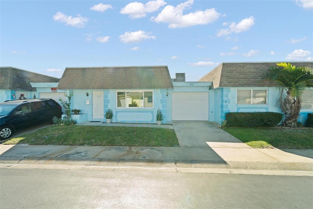 A light blue single-story house features a white garage door and a small front lawn — 7050 VERSAILLES N, PINELLAS PARK, FL