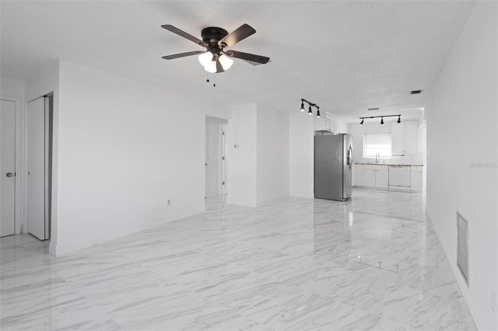 An open-concept living area features white marble-look tile flooring, a ceiling fan, and a kitchen — 7050 VERSAILLES N, PINELLAS PARK, FL