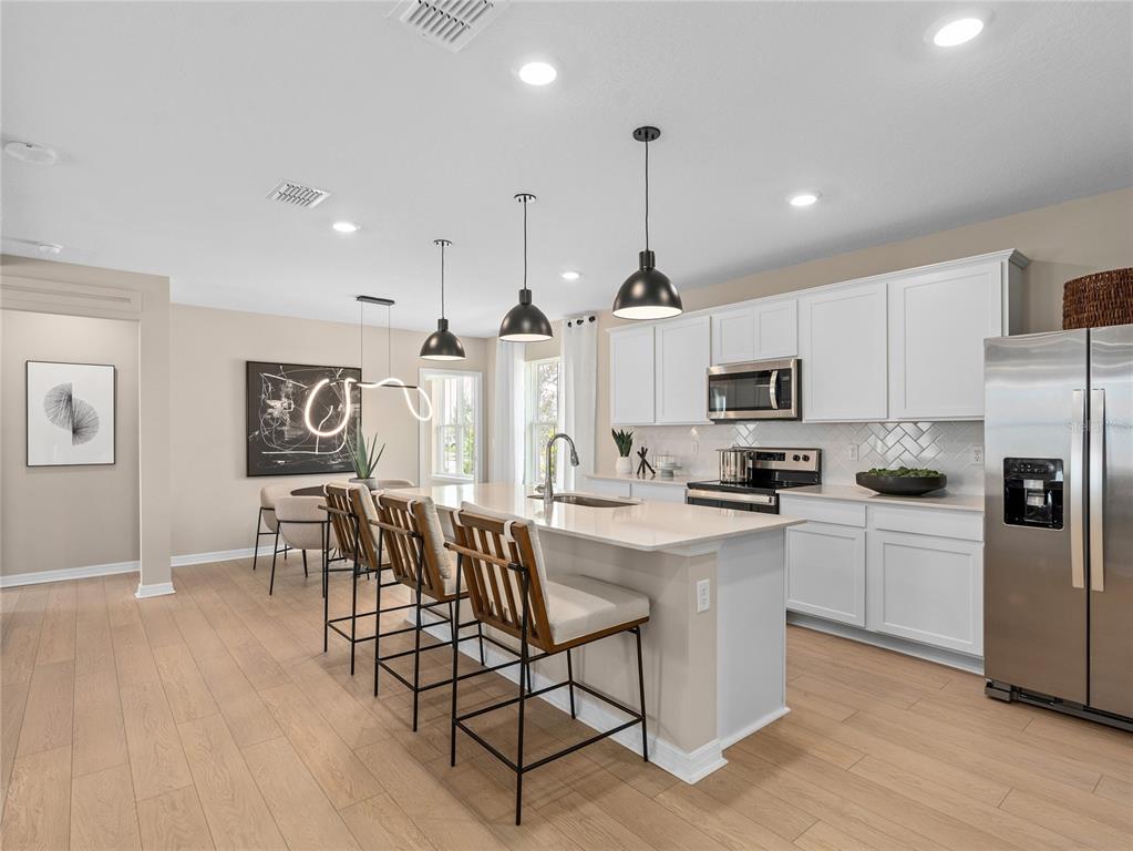 A modern kitchen features white cabinets, a quartz island with bar stools, and light flooring — 10710 LEAFY LAUREL STREET, ORLANDO, FL