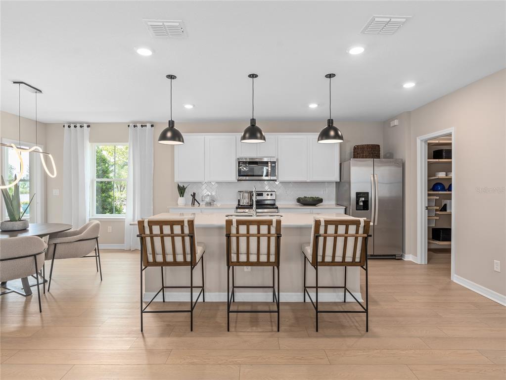A modern kitchen features white cabinetry, a central island with three stools, and stainless appliances — 10710 LEAFY LAUREL STREET, ORLANDO, FL